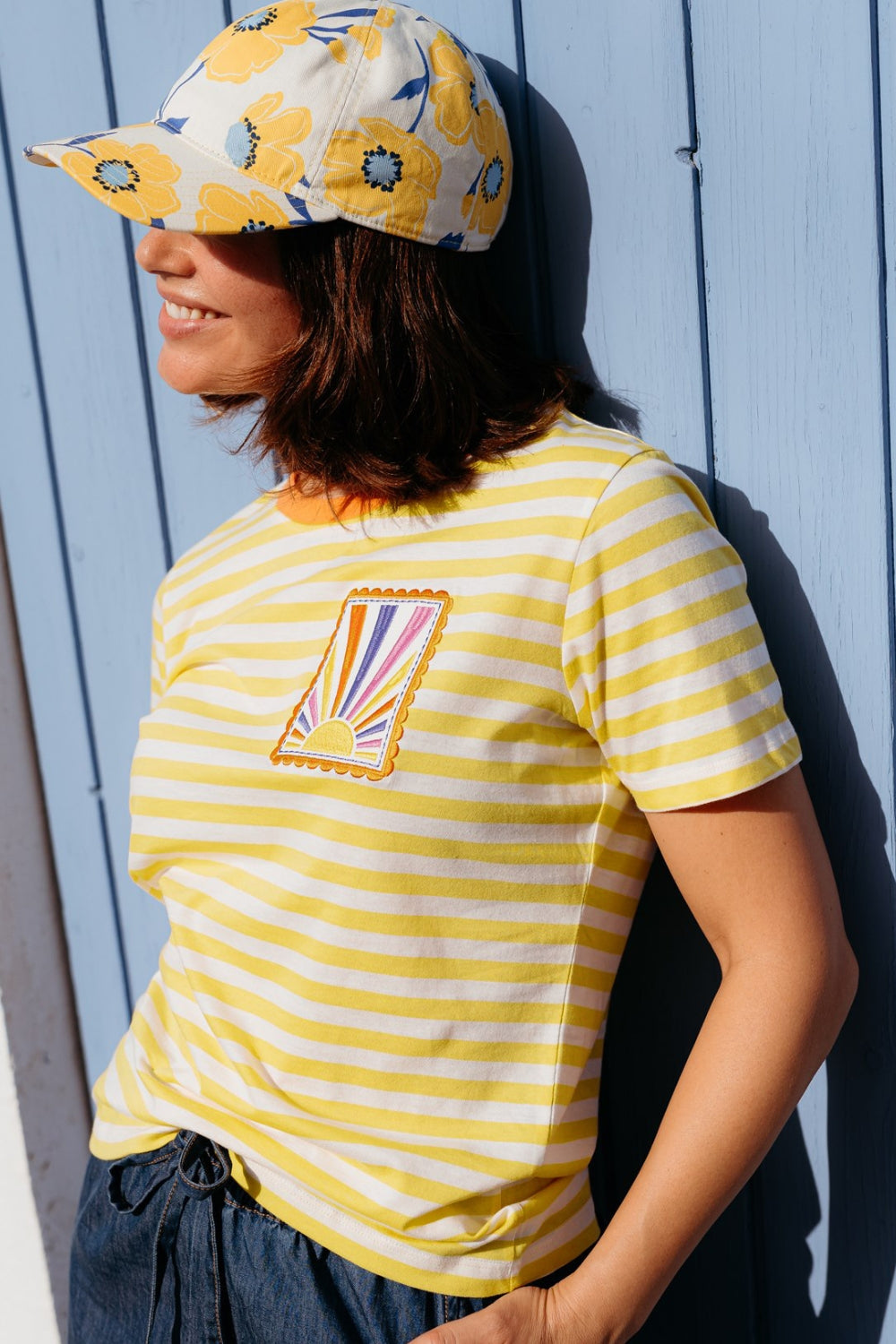 Person wearing a yellow and white striped shirt with a colorful graphic and a matching cap against a light blue wooden background.