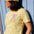 Person wearing a yellow and white striped shirt with a colorful graphic and a matching cap against a light blue wooden background.