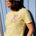 Person wearing a yellow and white striped shirt with a colorful graphic and a matching cap against a light blue wooden background.