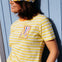 Person wearing a yellow and white striped shirt with a colorful graphic and a matching cap against a light blue wooden background.