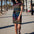 A model wearing a short-sleeved black mini dress with a colorful striped pattern and pockets, standing on a street with palm trees in the background.