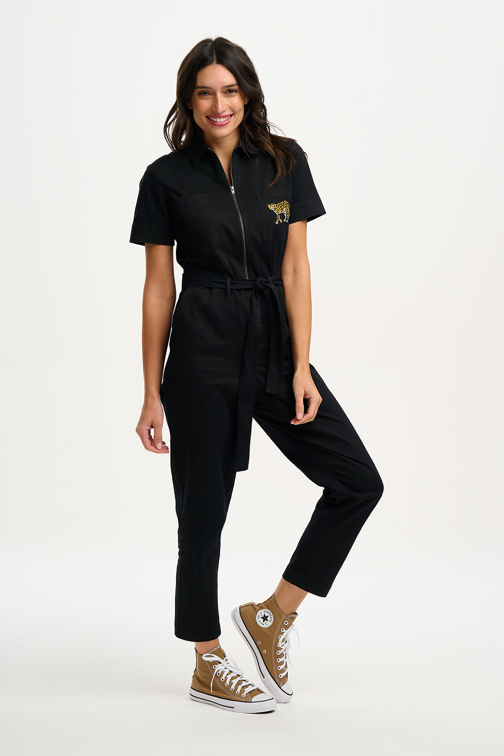 A woman wearing a black boilersuit with a leopard pocket, paired with light-colored sneakers.