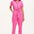 A model wearing a vibrant pink tailored boilersuit with straight legs, half sleeve shirt upper, and an exposed front zip. The suit features contrast cherry embroidery on the bust pocket and is styled with side seam pockets and a tie belt.