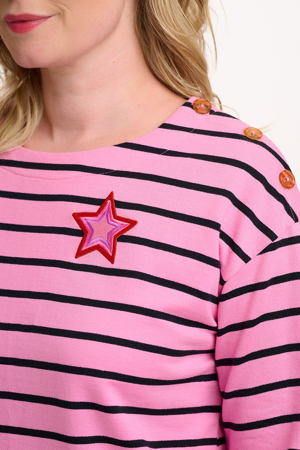 Sugarhill Brighton close-up of a pink and black striped shirt with a star-shaped brooch.