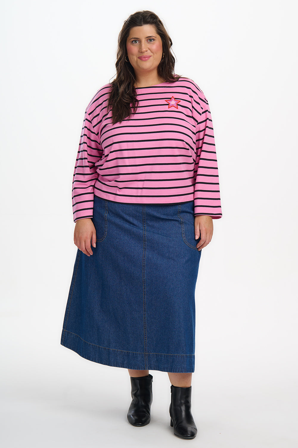 Woman wearing a pink and black striped sweater and blue denim skirt on a white background