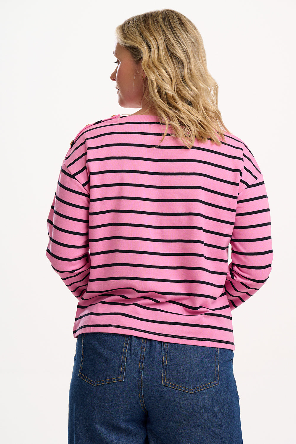 Sugarhill Brighton model wearing a pink and black striped shirt with blue jeans on a white background