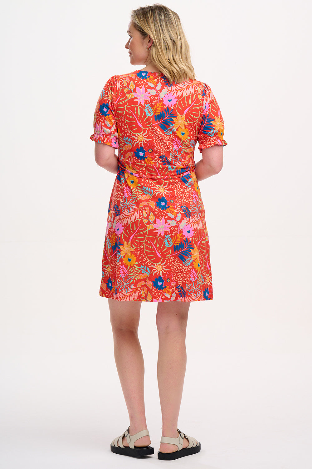 A model wearing a red fit and flare jersey mini dress with a colorful floral pattern, short shirred sleeves, and a round neckline.