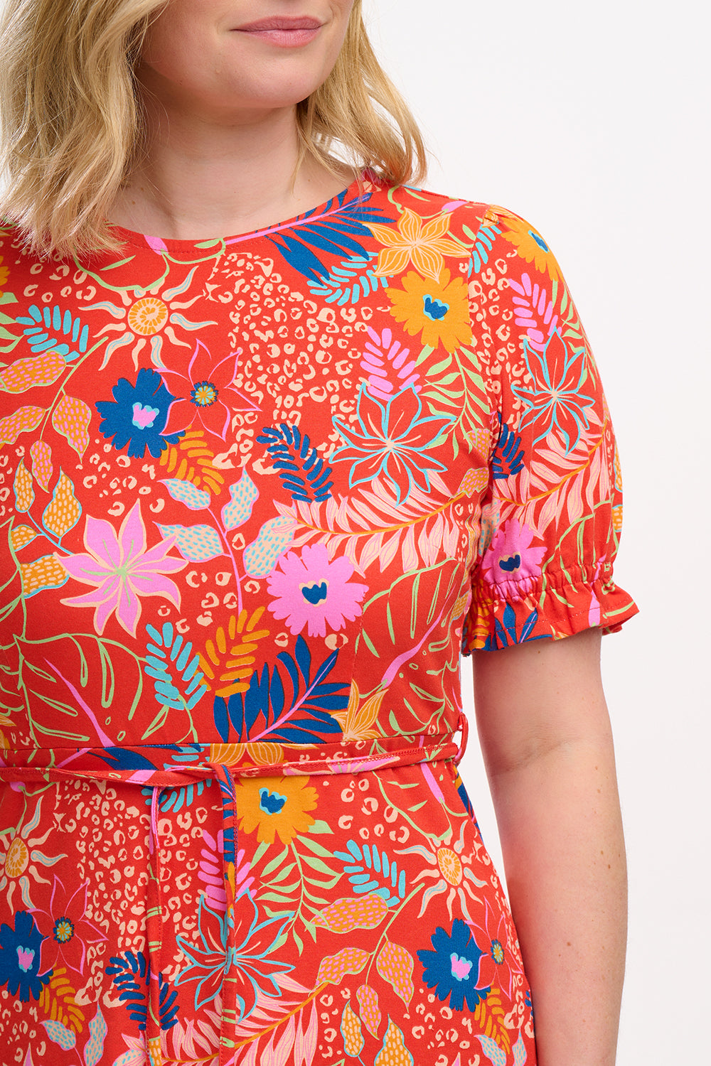 A model wearing a red fit and flare jersey mini dress with a colorful floral pattern, short shirred sleeves, and a round neckline.