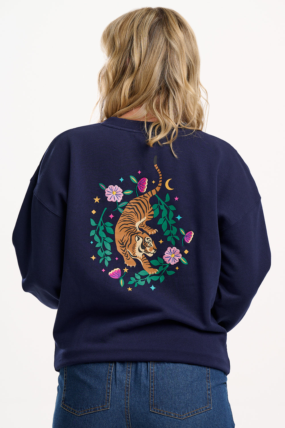 Person wearing a navy blue sweatshirt with a tiger design on the back, standing against a white background.