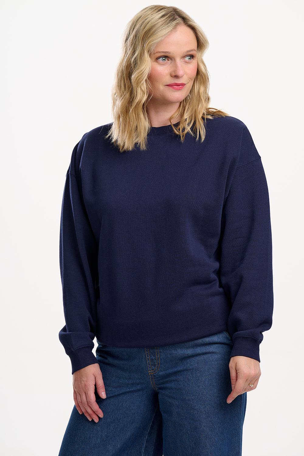 Woman wearing a navy blue sweater and jeans on a white background