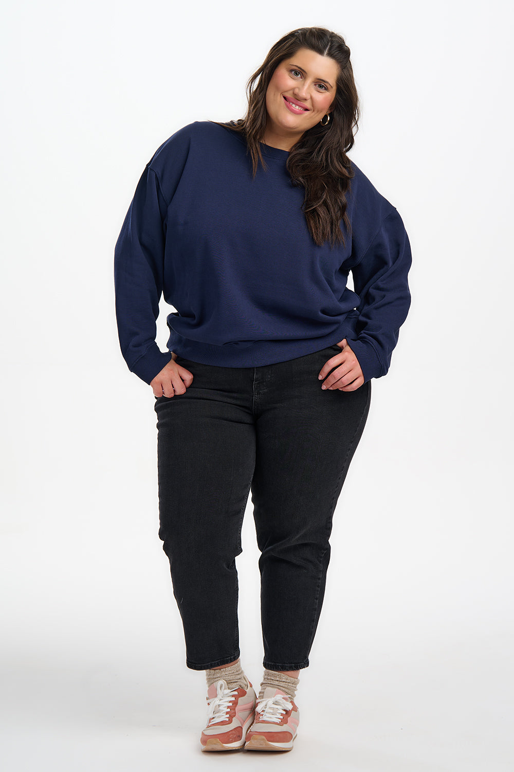 Woman wearing a navy blue sweater and black jeans on a white background