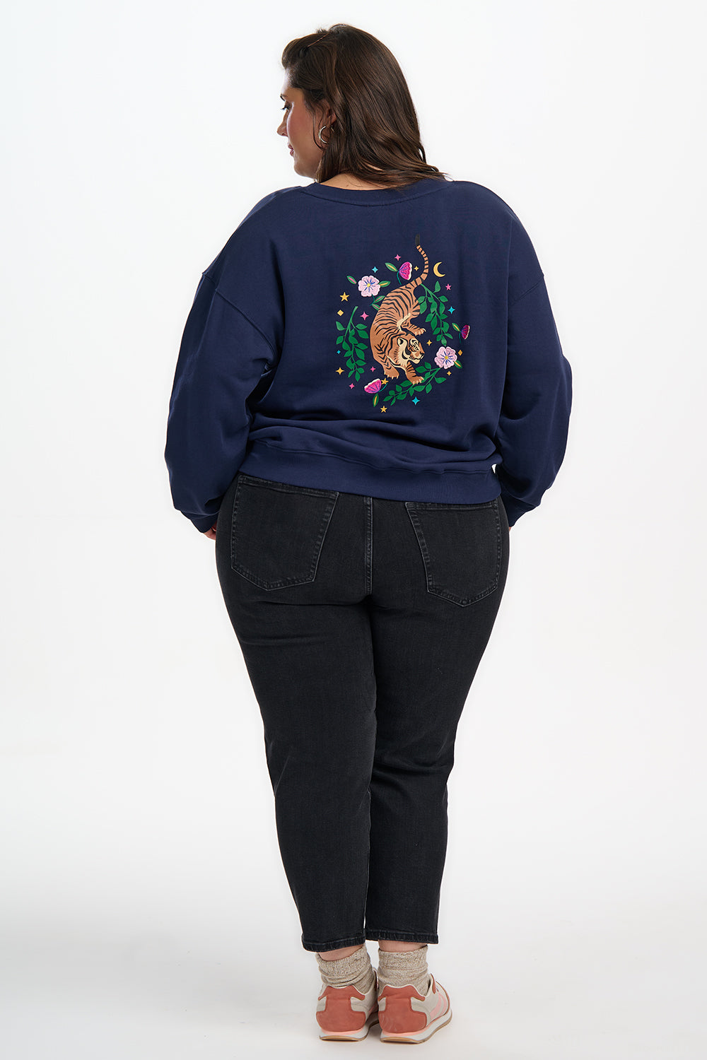 Person wearing a navy blue sweatshirt with a colorful design on the back, standing against a white background.