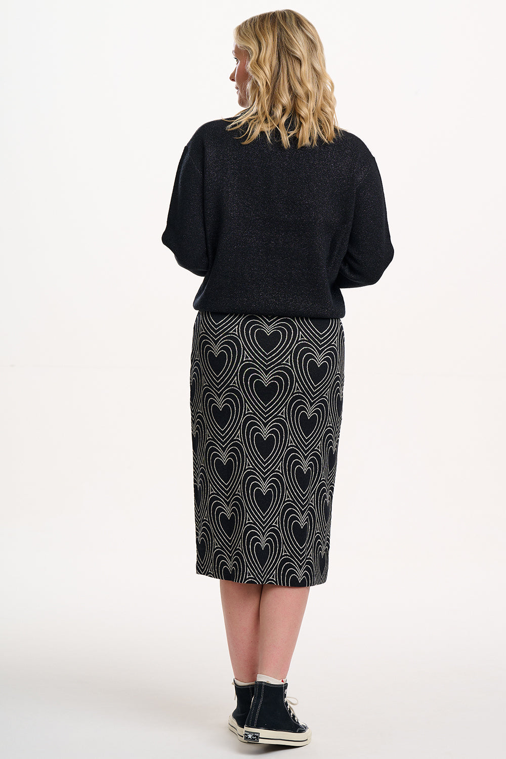 Person wearing a black sweater and patterned skirt on a white background