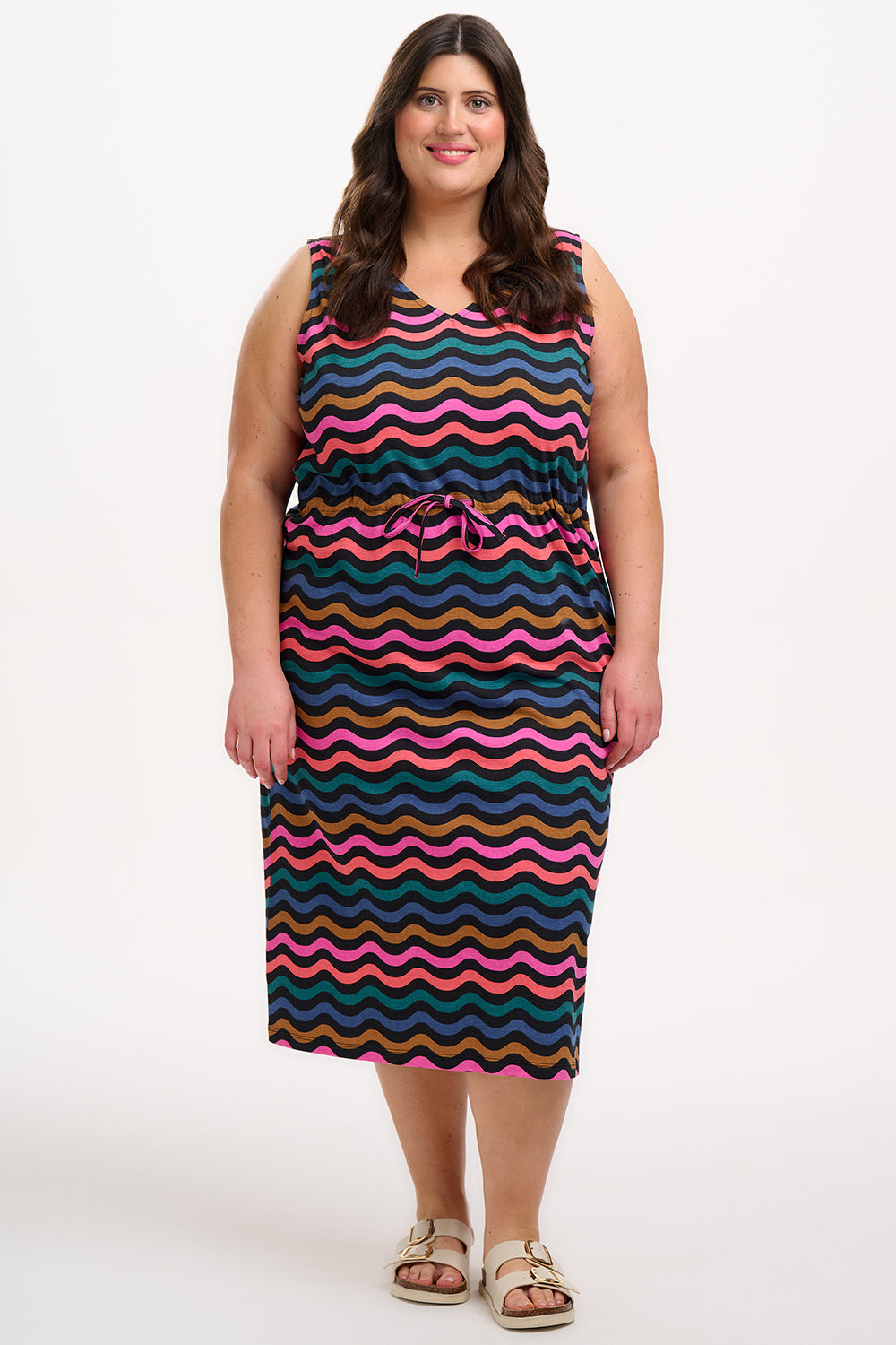 A model wearing a sleeveless midi dress with a wavy chevron stripe pattern in black, teal, navy, tan, pink, and coral colors.