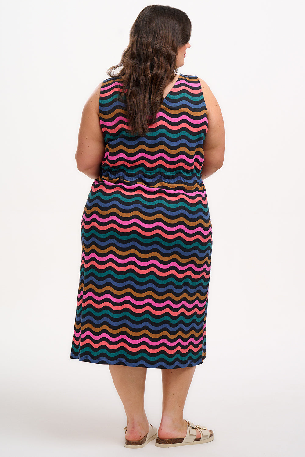 A model wearing a sleeveless midi dress with a wavy chevron stripe pattern in black, teal, navy, tan, pink, and coral colors.