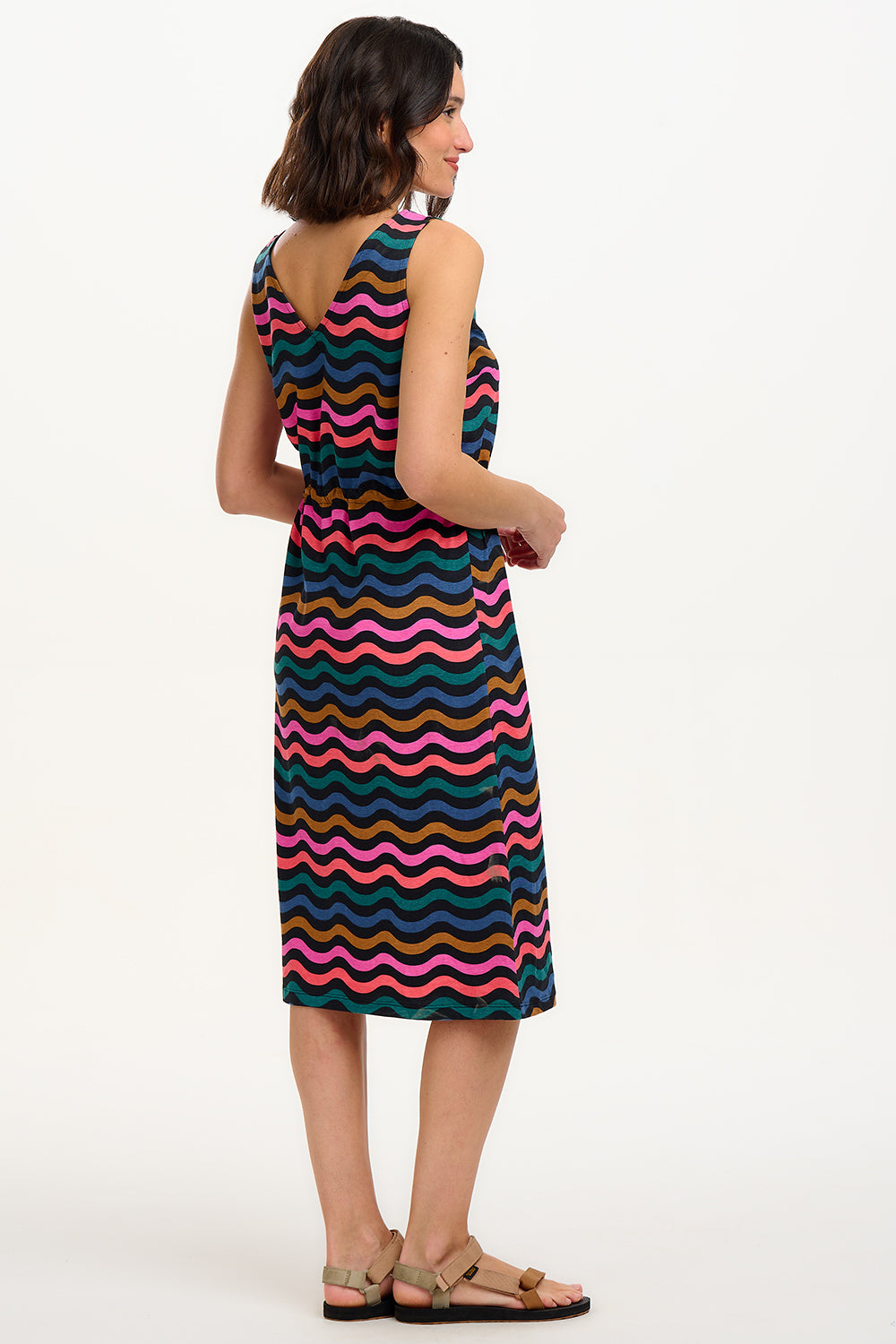 A model wearing a sleeveless midi dress with a wavy chevron stripe pattern in black, teal, navy, tan, pink, and coral colors.