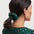 Woman with a green scrunchie in her hair wearing a green top with colorful polka dots on a white background