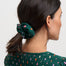 Woman with a green scrunchie in her hair wearing a green top with colorful polka dots on a white background