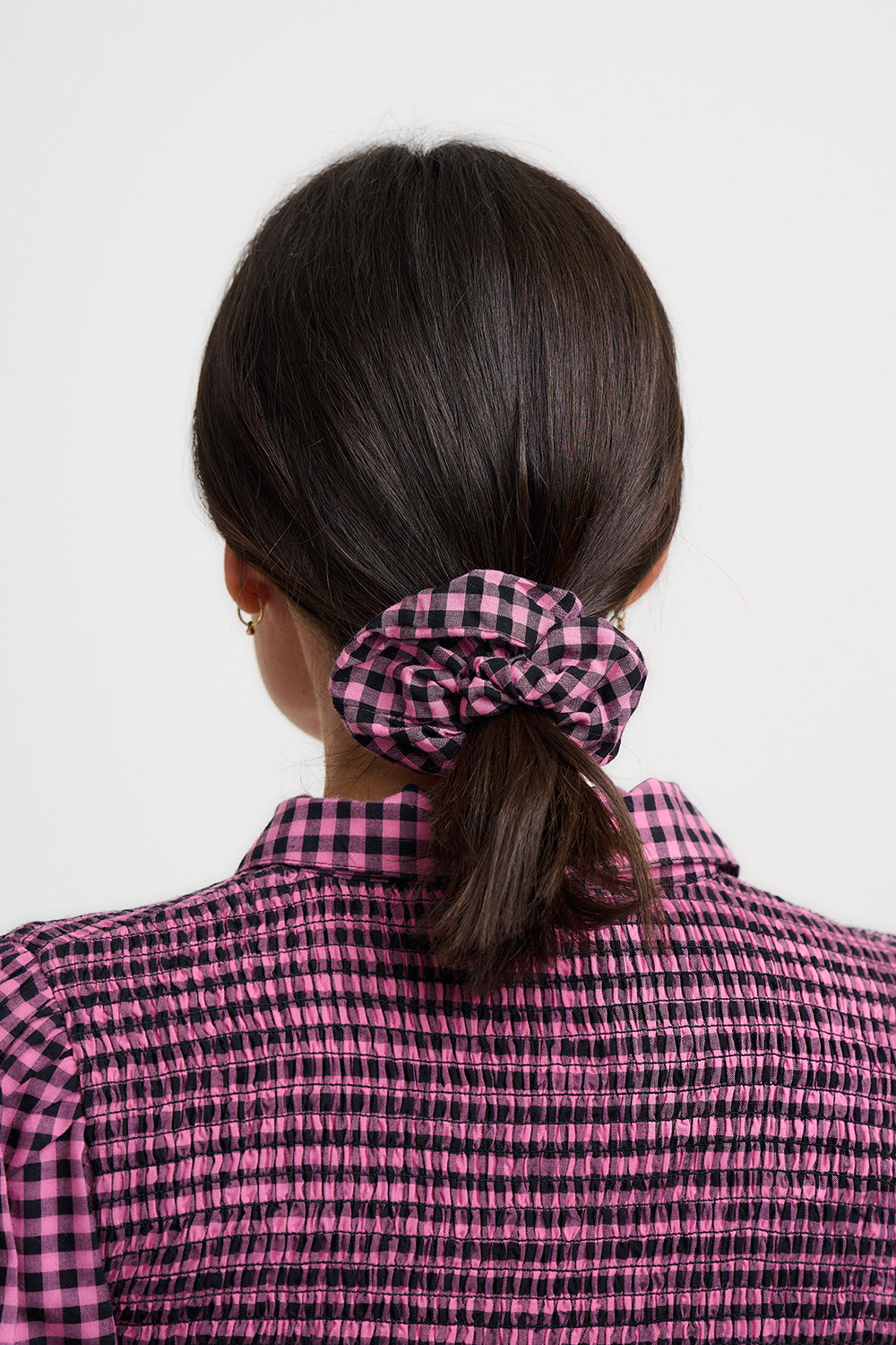 Person wearing a pink and black checkered shirt with a hair scrunchie in their hair.