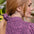 A close-up side profile of a woman with long strawberry blonde hair wearing a pink and black gingham shirt and a matching pink scrunchie.