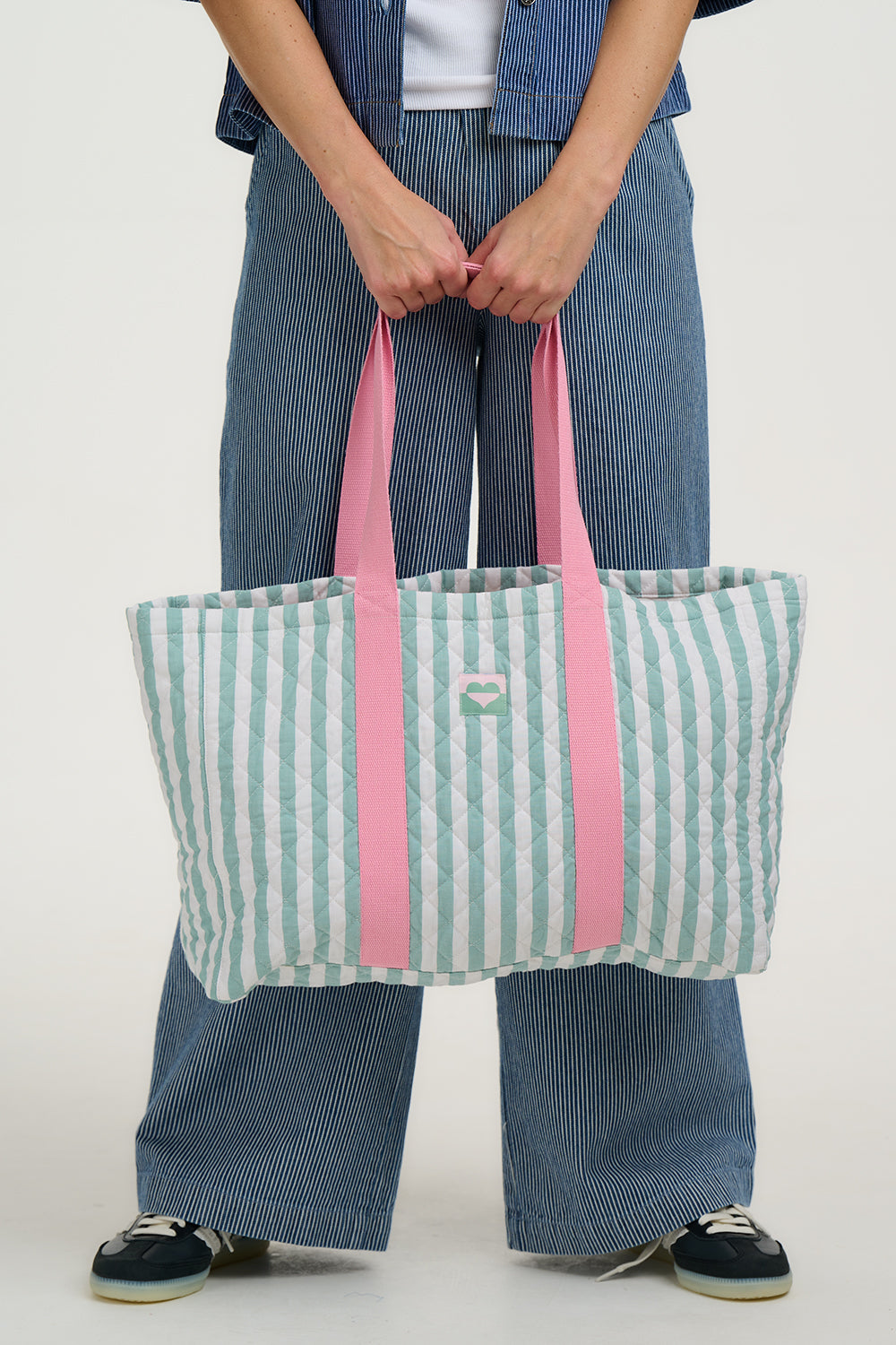 Person holding a striped tote bag with pink straps against a white background