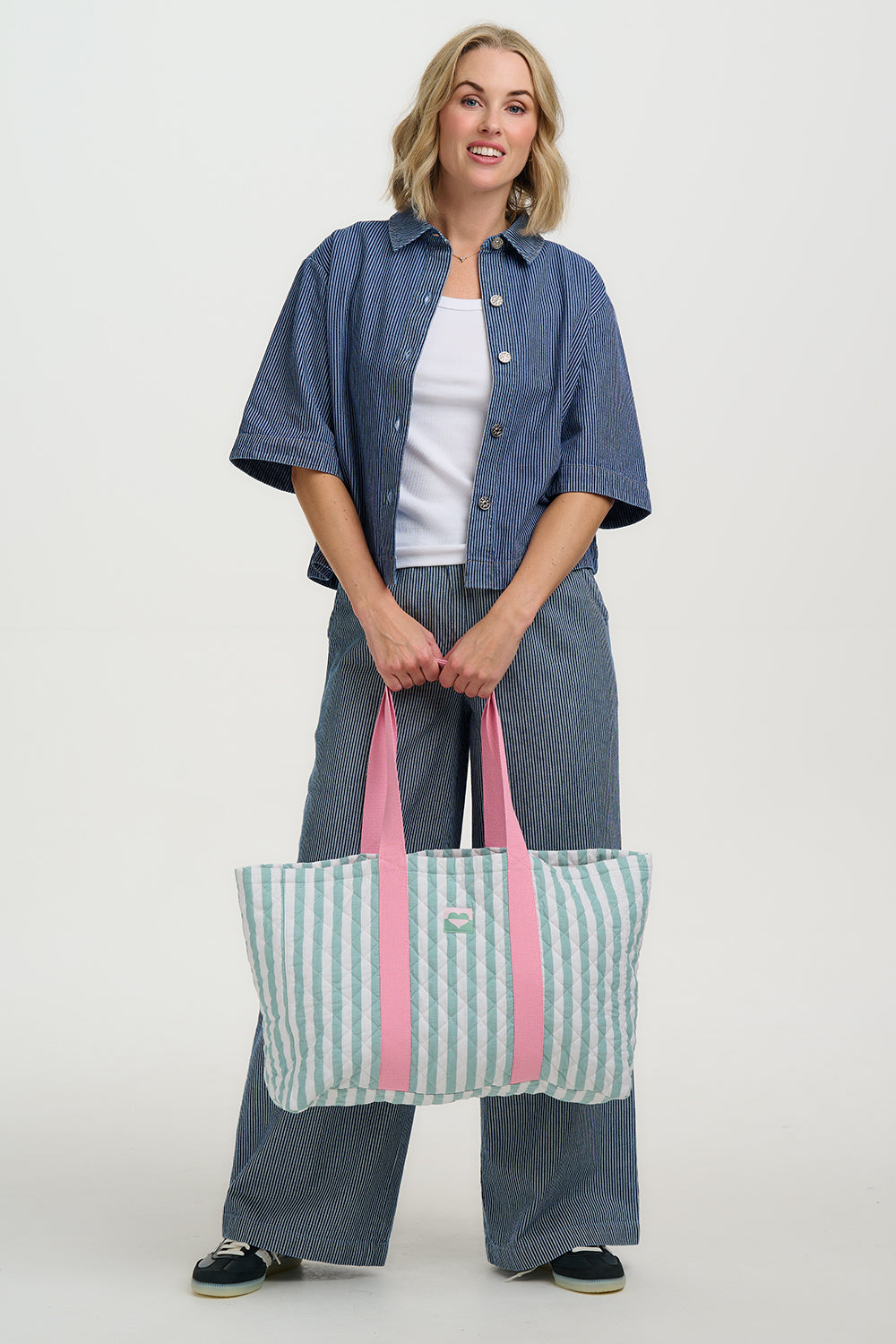 Woman holding a striped tote bag with pink straps on a white background