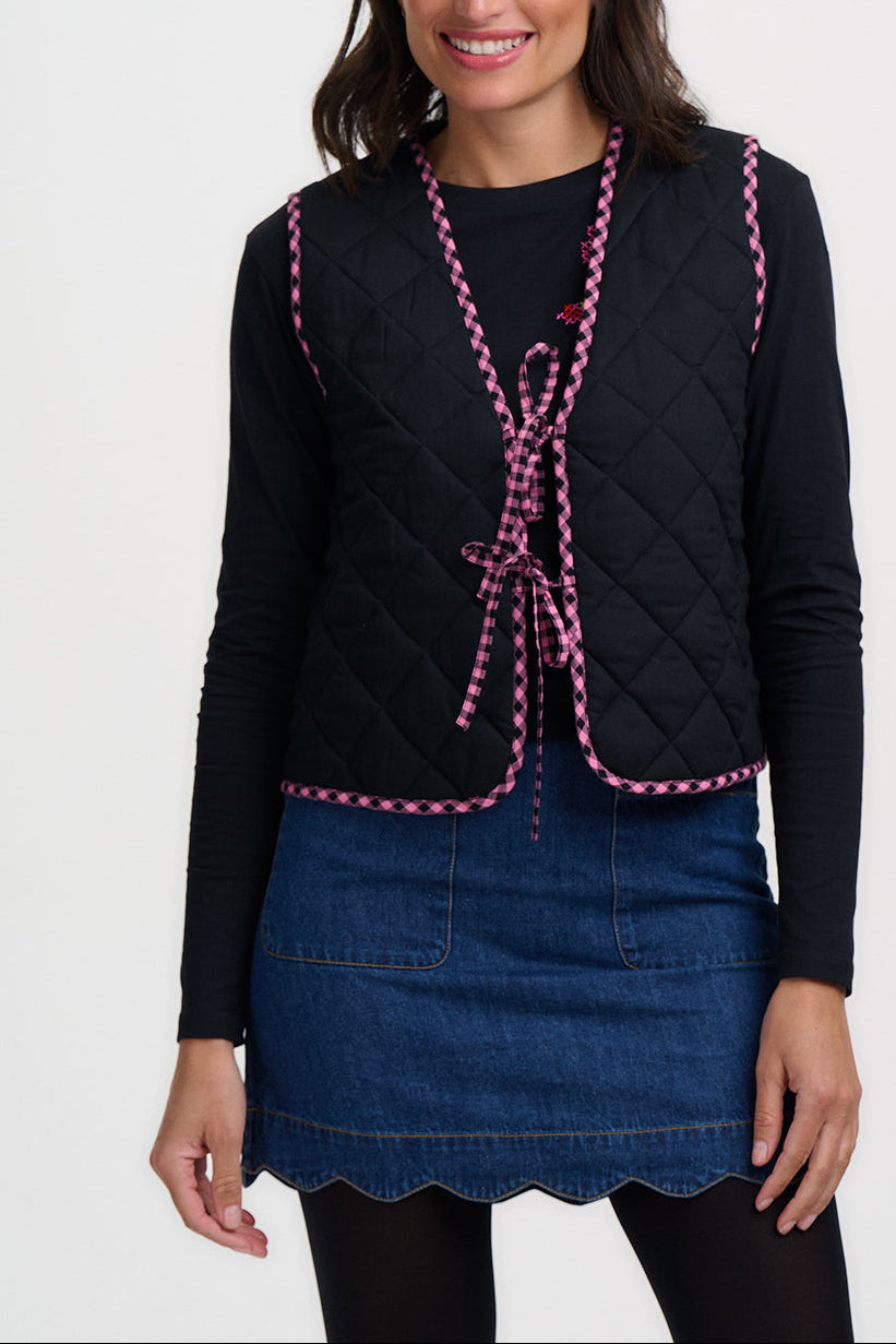 Woman wearing a black quilted vest with pink trim on a white background