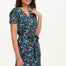 A model wearing a short-sleeved V-neck jersey mini dress with a floral and dinosaur print in various colors on a teal background.