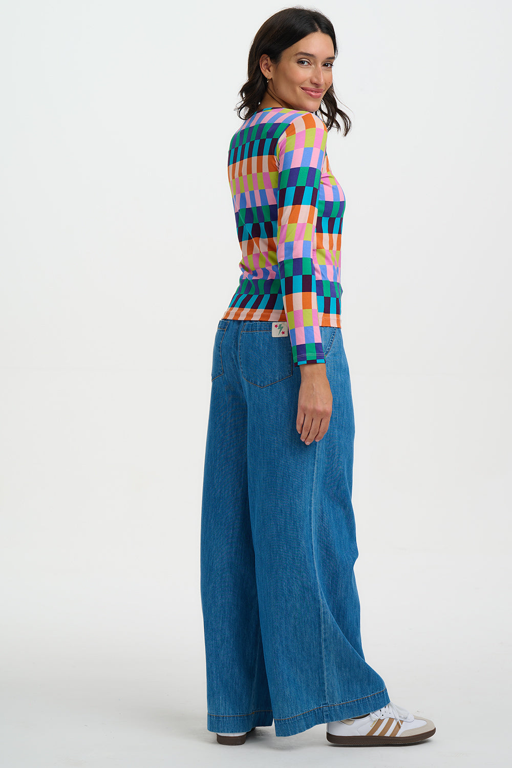 Woman wearing a colorful checkered sweater and blue jeans on a white background