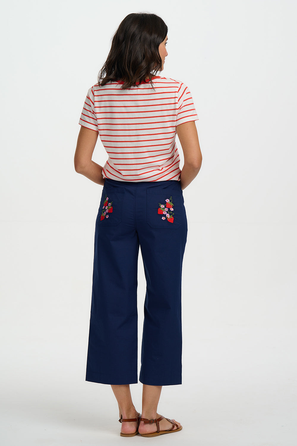 Woman wearing a striped shirt and navy pants with floral embroidery on a white background