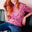 Person with red hair wearing a pink polka dot shirt and blue jeans sitting on a green couch.