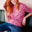 Person with red hair wearing a pink polka dot shirt and blue jeans sitting on a green couch.