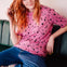 Person with red hair wearing a pink polka dot shirt and blue jeans sitting on a green couch.