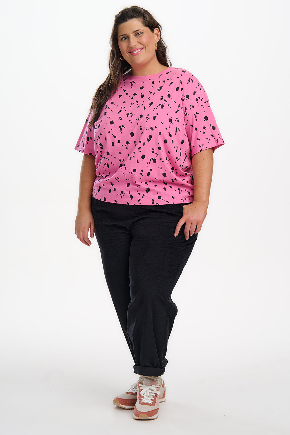 Woman wearing a pink top with black patterns and black pants on a white background