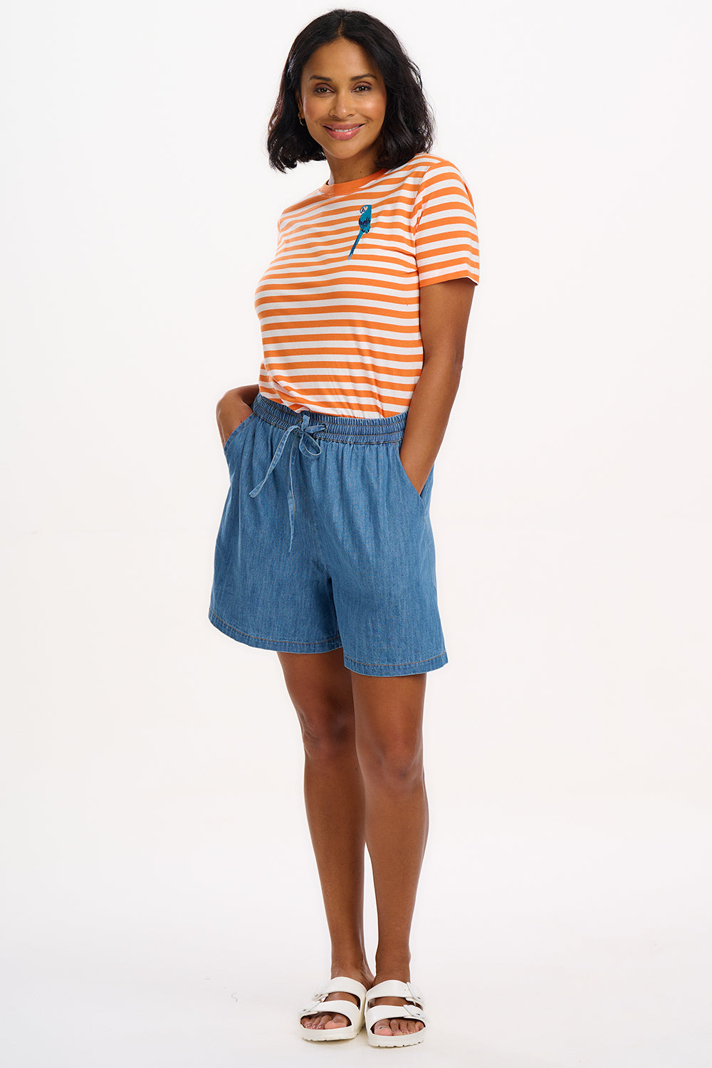 Person wearing an orange and white striped shirt with a blue parrot design, standing against a white background.