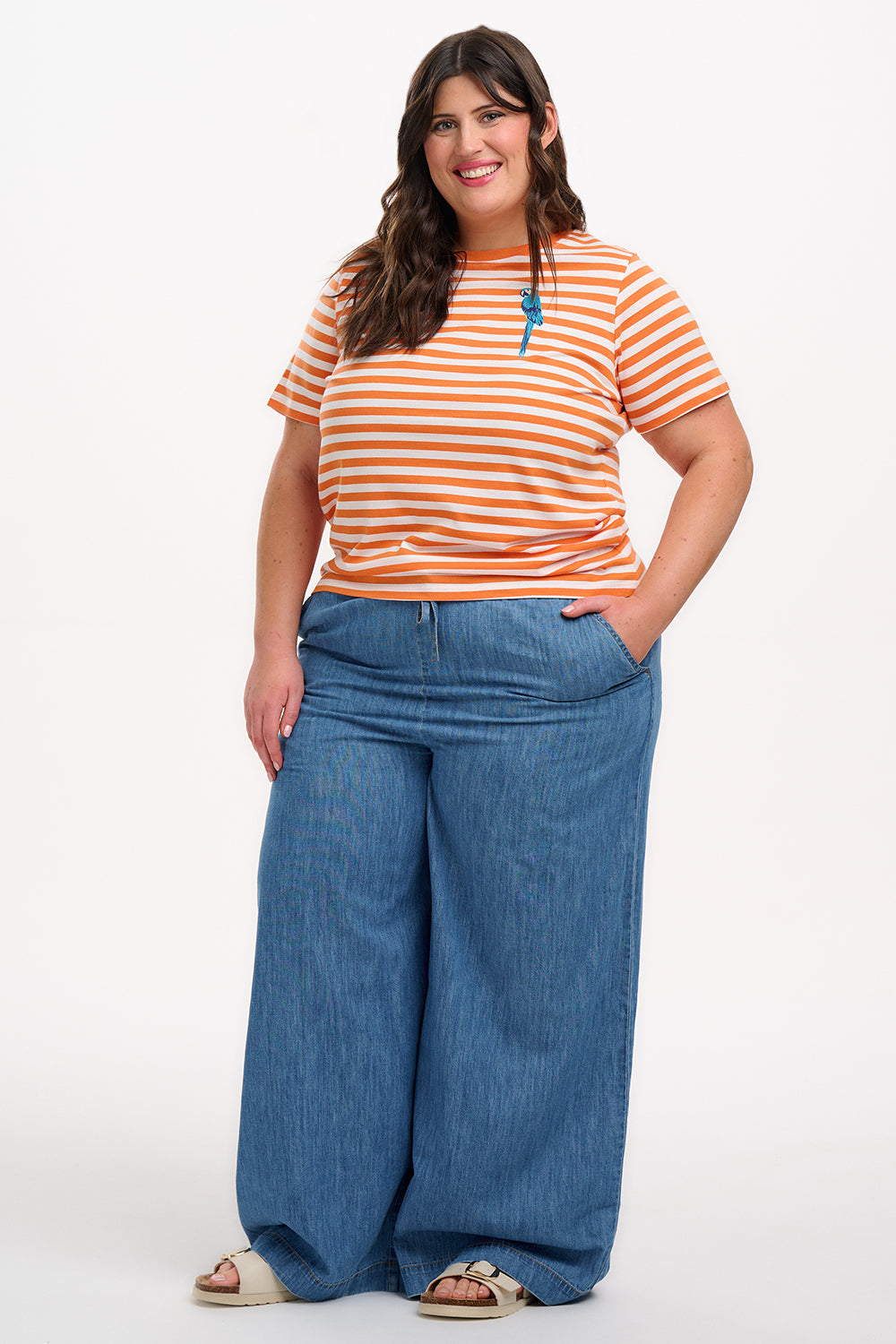Person wearing an orange and white striped shirt with a blue parrot design, standing against a white background.