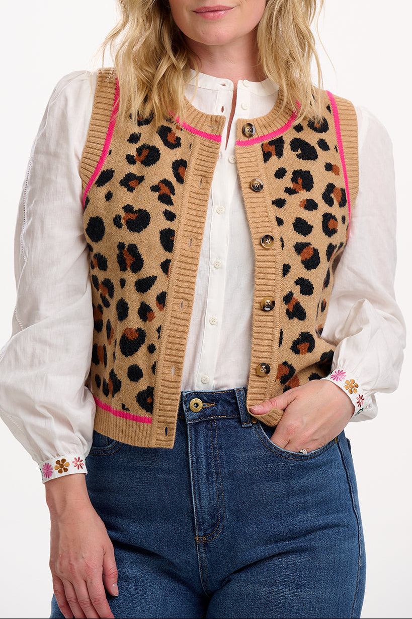 Sugarhill Brighton model wearing a leopard print cardigan with pink accents, white blouse, and blue jeans on a white background