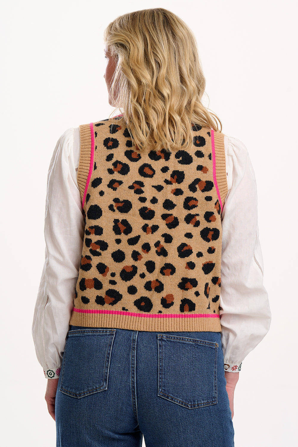 Sugarhill Brighton model wearing a leopard print vest with pink trim, white shirt, and blue jeans on a white background