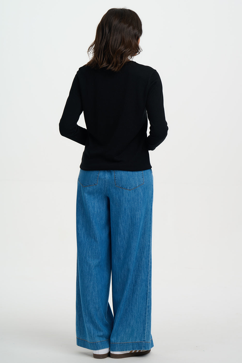 Person wearing a black top and blue jeans on a white background