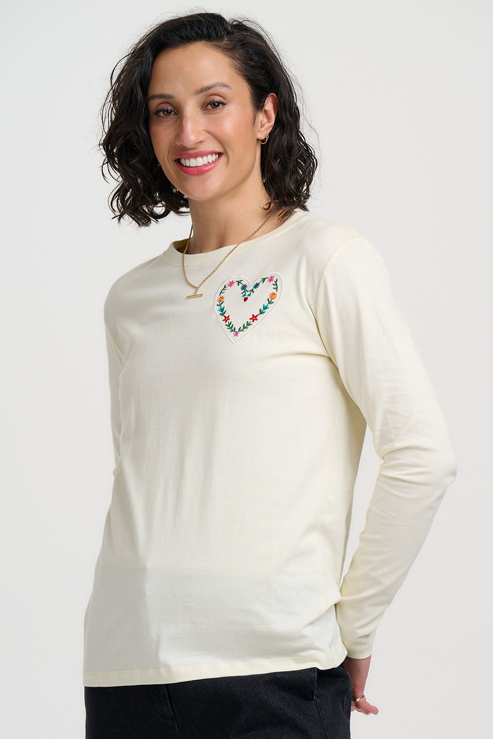 Woman wearing a cream long-sleeve shirt with a colorful heart design on a white background