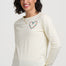 Woman wearing a cream long-sleeve shirt with a colorful heart design on a white background