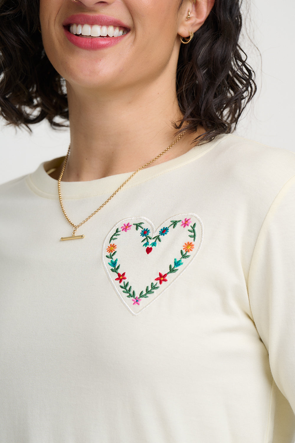 Woman wearing a cream-colored sweatshirt with a floral heart design on a white background