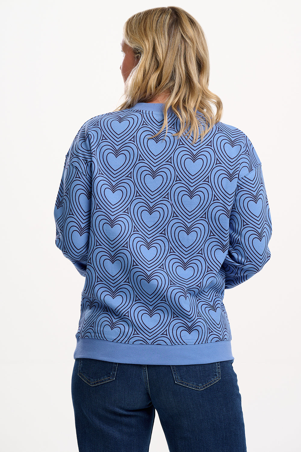 Sugarhill Brighton model wearing a blue sweater with heart pattern on a white background