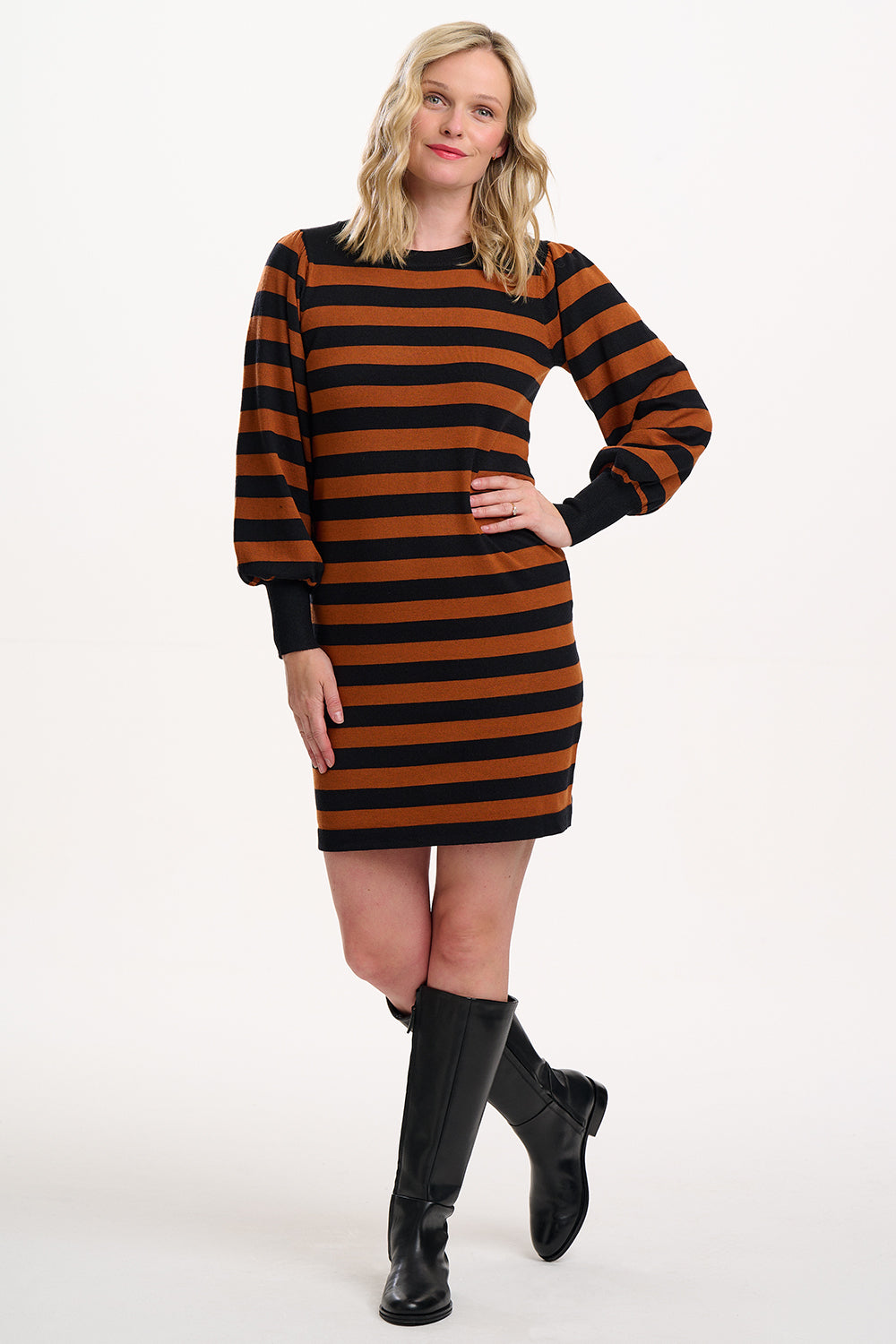 Woman wearing a black and orange striped dress with black boots on a white background