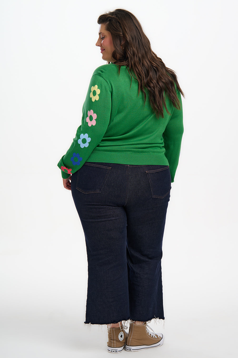 Person wearing a green sweater with floral designs and dark blue jeans on a white background