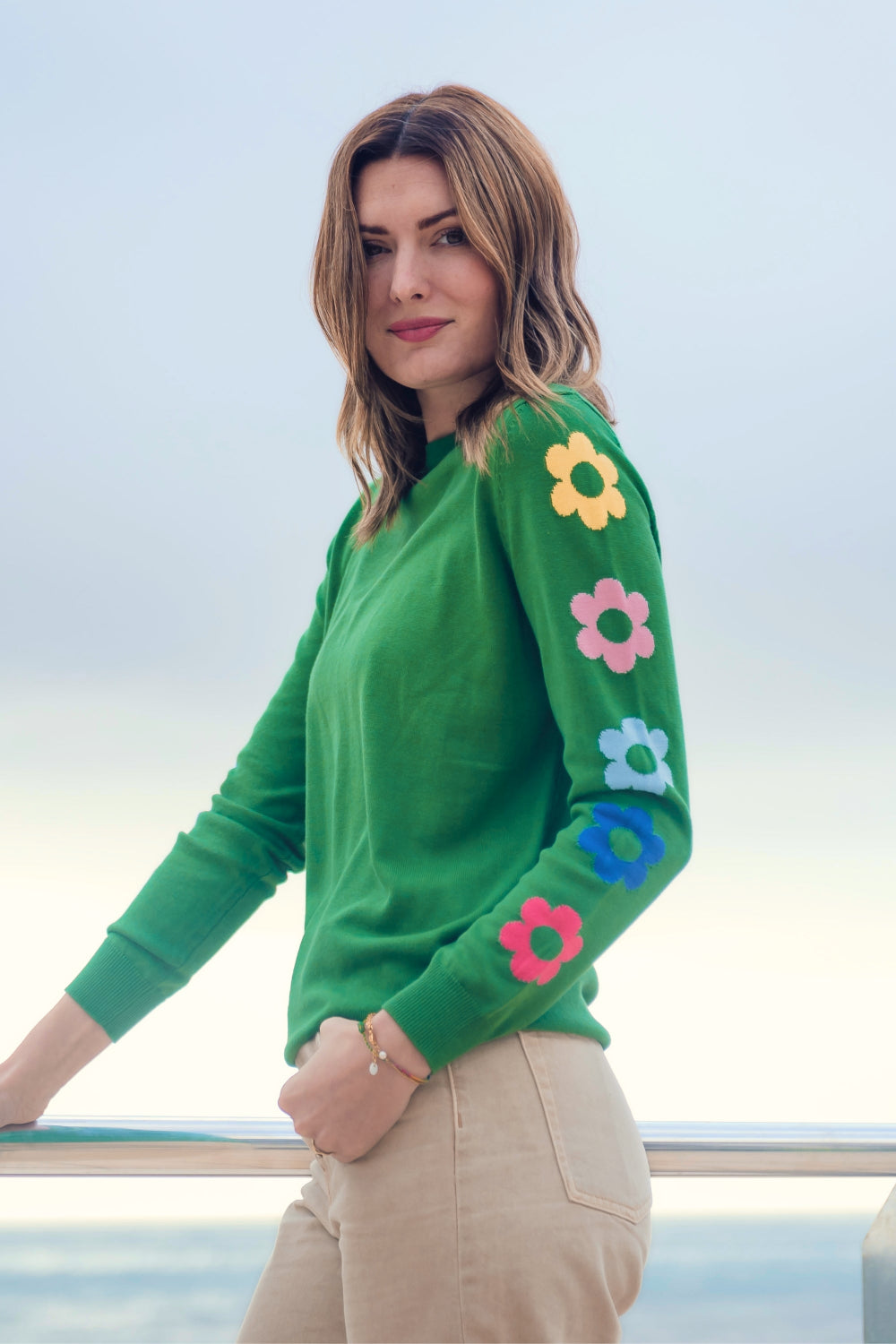 Sugarhill Brighton model wearing a green jumper with flower motifs on the sleeves, paired with cream jeans.
