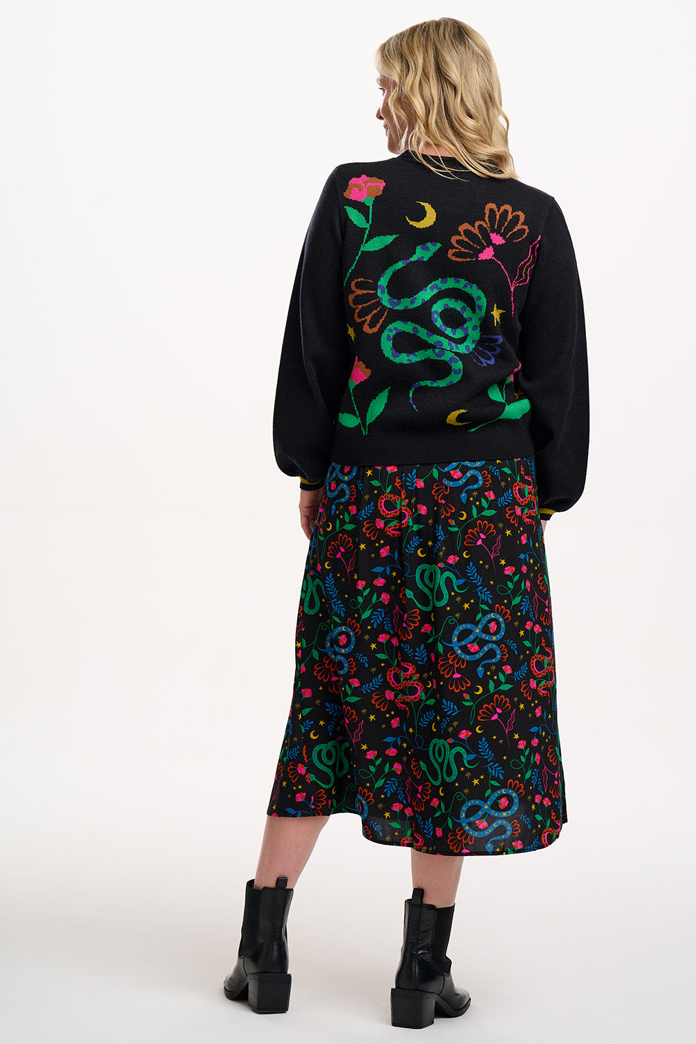 Woman wearing a black sweater and colorful skirt with snake design on a white background