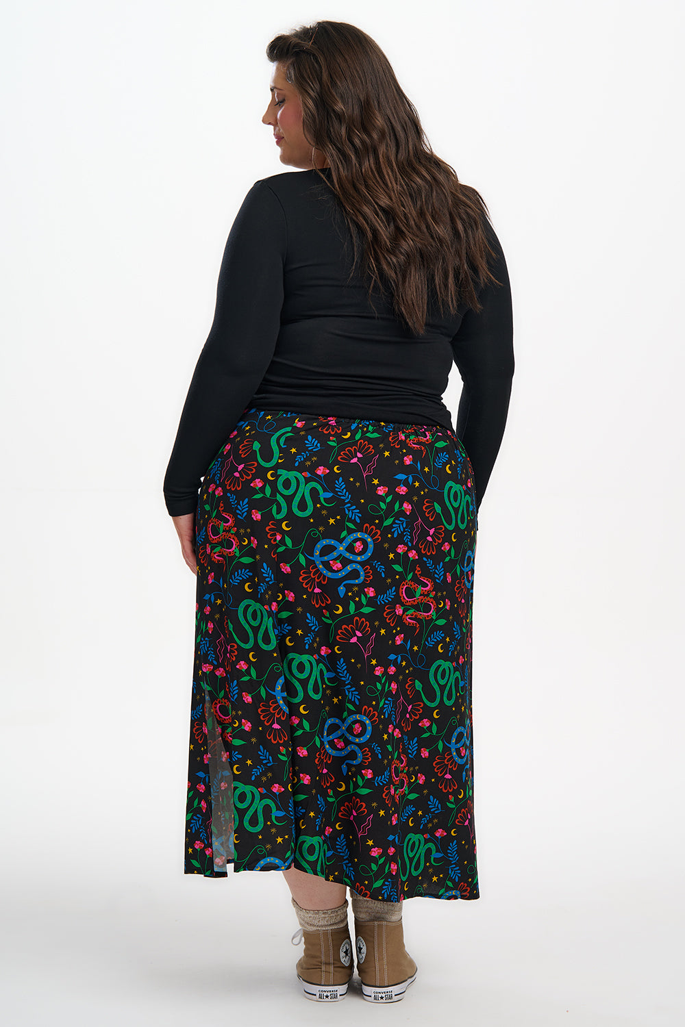 Woman wearing a black top and colorful patterned skirt on a white background