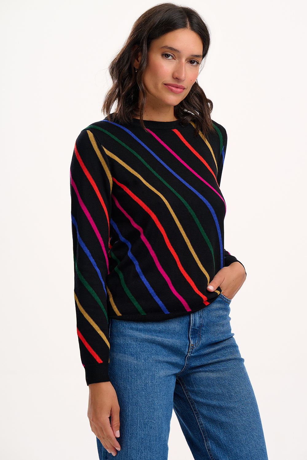 Woman wearing a black sweater with colorful stripes and blue jeans on a white background