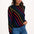 Woman wearing a black sweater with colorful stripes and blue jeans on a white background